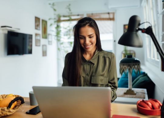 Happy attractive young woman of middle eastern ethnicity, working from home, using a laptop