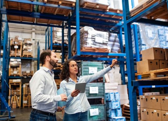 Businesswoman with a digital tablet showing and talking with male worker in distribution warehouse. Manager working with foreman in warehouse checking stock levels.